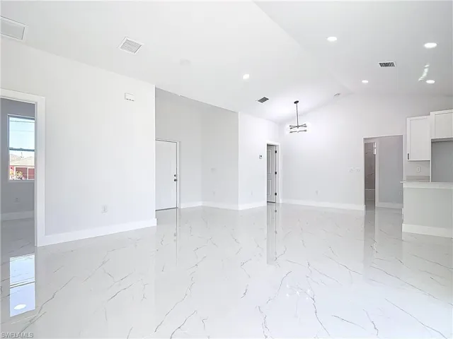 Spare room with lofted ceiling, a chandelier, recessed lighting, and light marble finish flooring