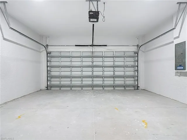 Garage with a textured wall, electric panel, and a garage door opener