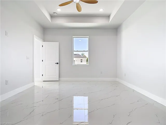 Empty room with light marble finish floors, a raised ceiling, and ceiling fan