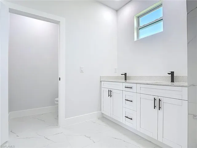 Full bath with double vanity and light marble finish floors