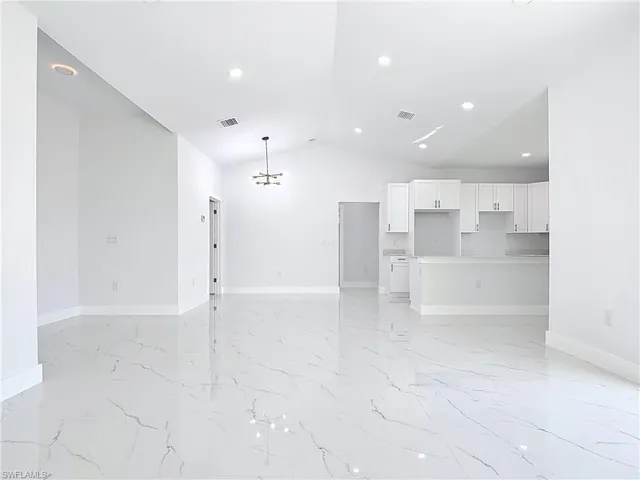 Unfurnished living room with a chandelier, vaulted ceiling, recessed lighting, and light marble finish floors