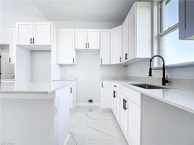 Kitchen featuring white cabinets, light stone countertops, and light marble finish flooring