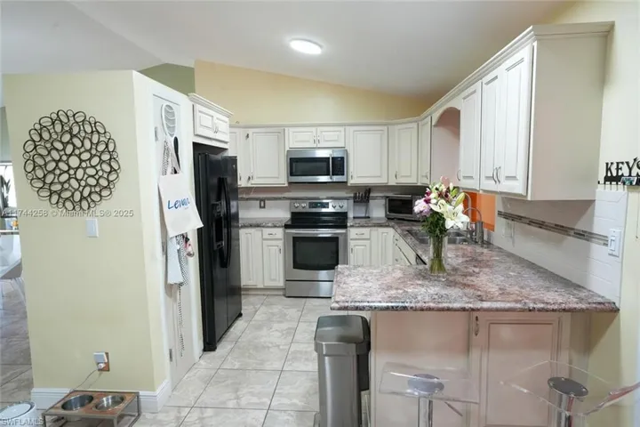 Kitchen featuring lofted ceiling, a peninsula, stainless steel appliances, white cabinets, and decorative backsplash
