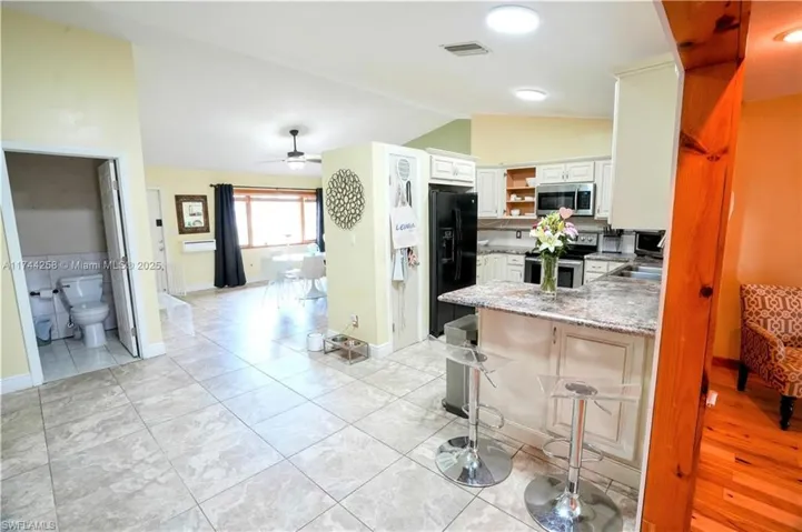 Kitchen with a peninsula, lofted ceiling, open shelves, appliances with stainless steel finishes, and ceiling fan