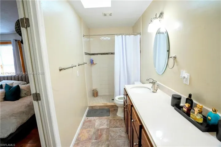 Full bath with vanity, a shower stall, a skylight, and light stone finish floors