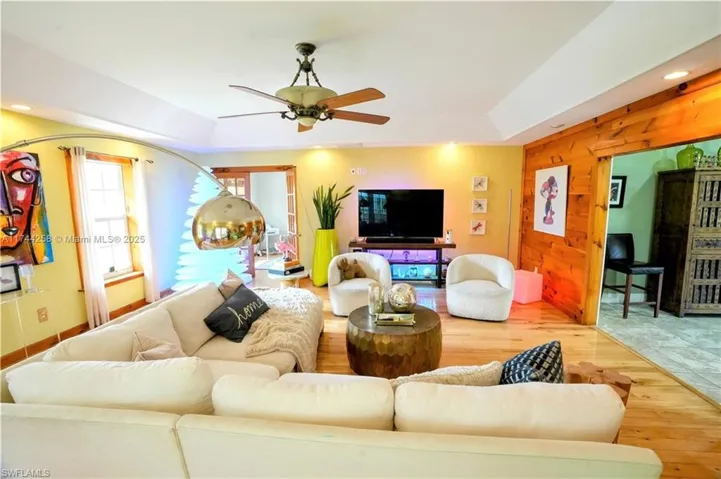 Living room with wood walls, a raised ceiling, wood finished floors, a ceiling fan, and recessed lighting