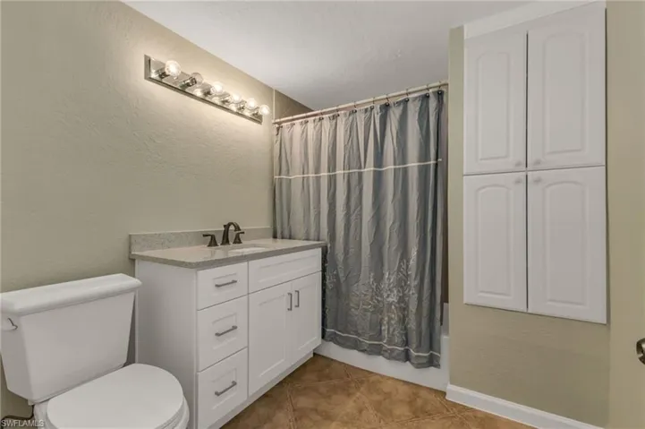 Bathroom with a textured wall, vanity, light tile patterned flooring, and shower / bath combo