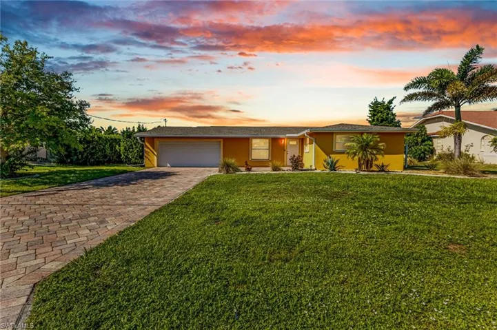 Ranch-style home featuring a yard, decorative driveway, an attached garage, and stucco siding