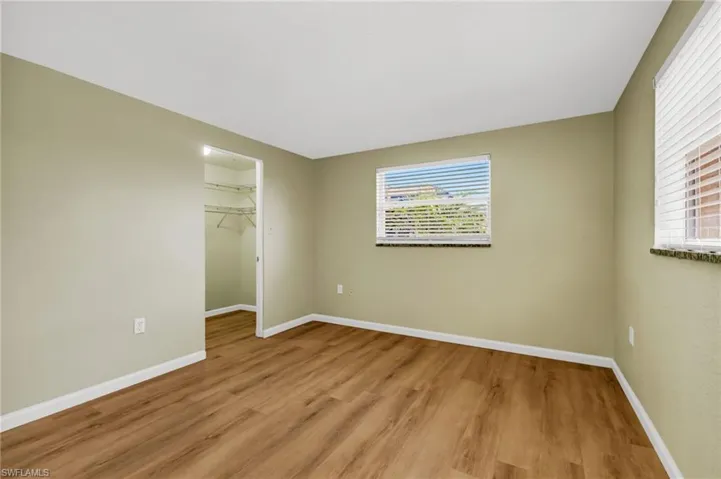 Unfurnished bedroom with multiple windows, a spacious closet, and light wood-style flooring