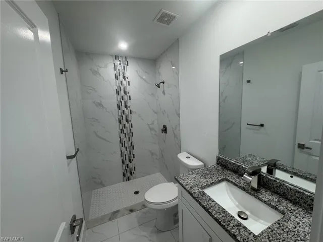Full bath with vanity, a marble finish shower, and light marble finish floors