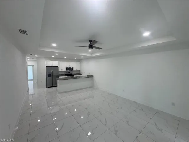 Unfurnished living room with recessed lighting, a raised ceiling, ceiling fan, and light marble finish floors