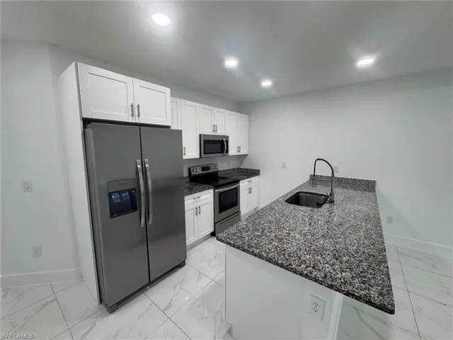 Kitchen featuring dark stone counters, appliances with stainless steel finishes, white cabinetry, a peninsula, and recessed lighting