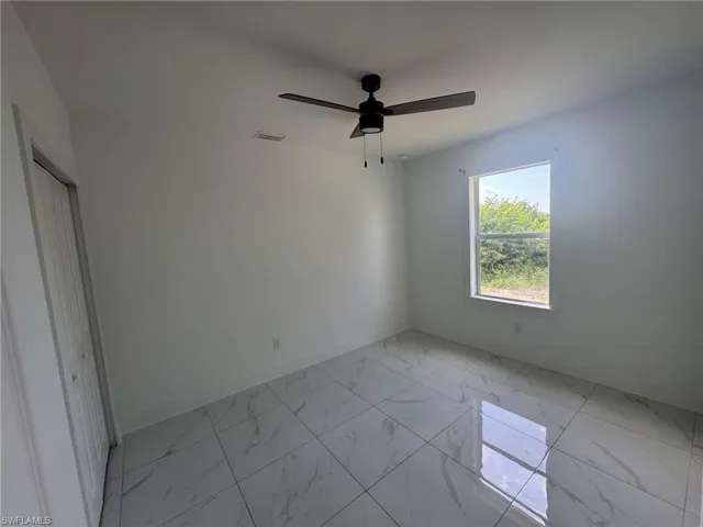 Unfurnished bedroom featuring light marble finish floors, ceiling fan, and a closet
