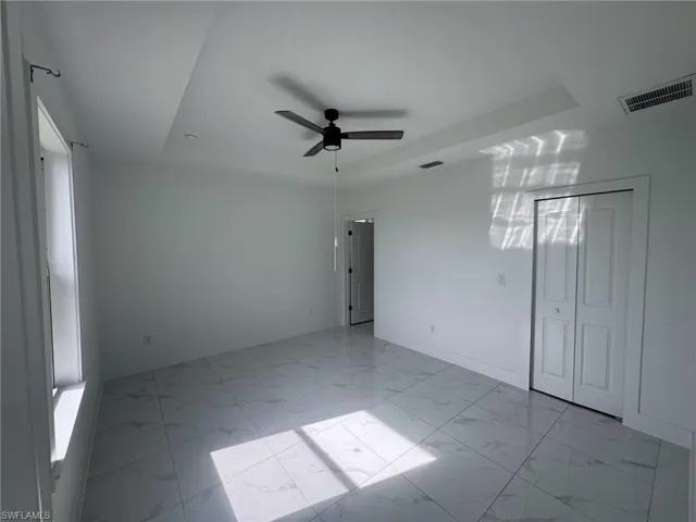Unfurnished room featuring a raised ceiling, a ceiling fan, and light marble finish flooring