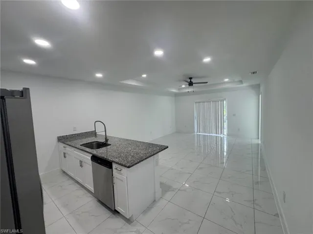 Kitchen with a peninsula, dark stone counters, white cabinets, a raised ceiling, and light marble finish floors