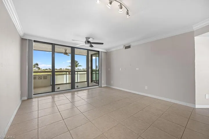 Tiled spare room featuring track lighting, expansive windows, ornamental molding, and ceiling fan