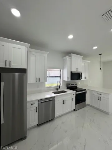 Kitchen with light marble finish flooring, refrigerator, stainless steel range, hanging light fixtures, and white cabinets