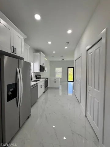 Kitchen featuring refrigerator, white cabinetry, light marble finish floors, range, and recessed lighting