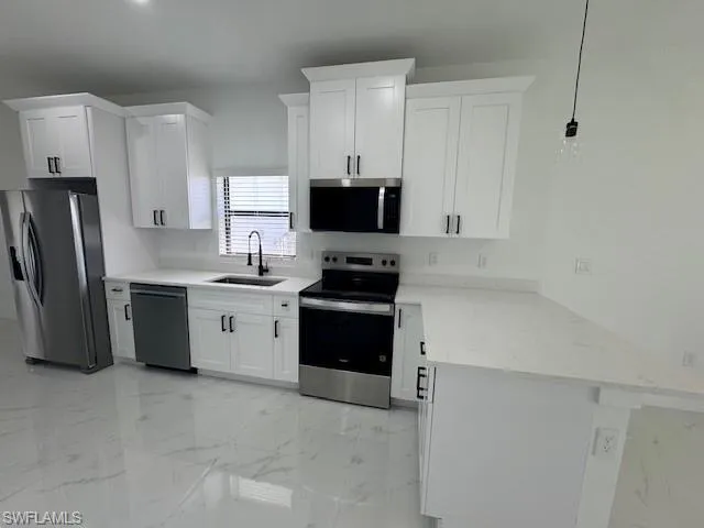 Kitchen featuring a peninsula, appliances with stainless steel finishes, light marble finish flooring, white cabinetry, and light stone counters