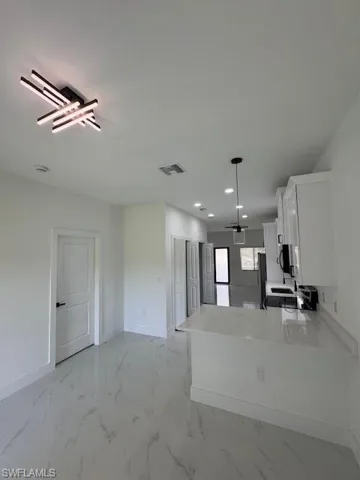 Kitchen featuring white cabinets, light marble finish floors, light stone counters, decorative light fixtures, and recessed lighting