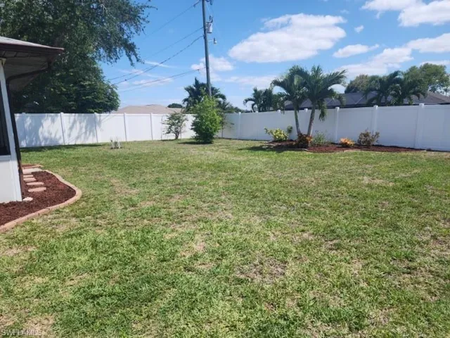 Expansive backyard featuring a manicured lawn, a white privacy fence, and mature palm trees
