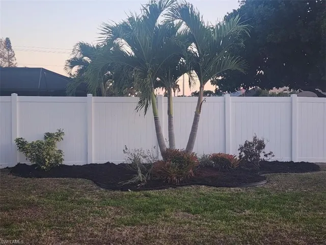 Manicured lawn with a white privacy fence, mature palm trees, and dark mulch landscaping beds