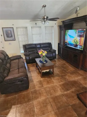 Spacious living area featuring large format floor tiles, vaulted ceiling, and a ceiling fan with integrated lighting