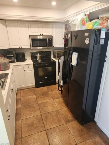 Kitchen featuring white cabinetry with dark hardware, a stainless steel microwave, black electric range, and tile flooring