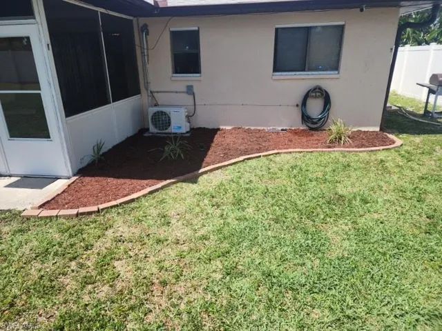 Landscaped planting bed with decorative mulch and brick edging, complemented by a screened patio enclosure and a stucco exterior