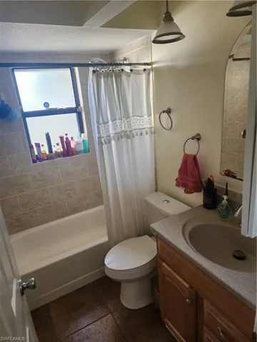 Bathroom featuring a white bathtub with tile surround, wood-finish vanity with an integrated sink, and dark-toned floor tiles