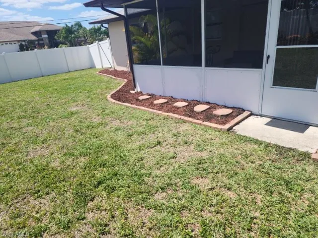Expansive lawn with a white privacy fence, featuring a screened patio and a mulched garden bed with stepping stones
