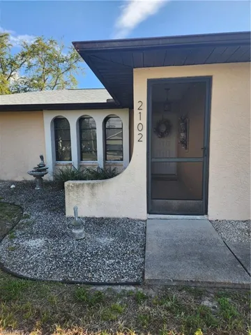 Stucco exterior featuring arched windows with black frames, a screened entry door, and a gravel-covered front yard