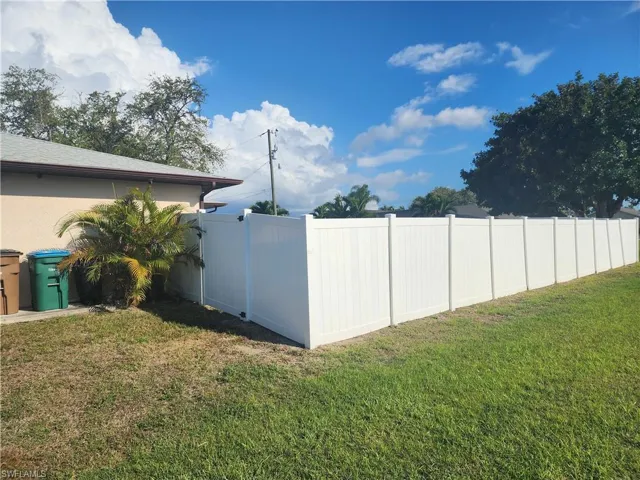 Spacious side yard featuring a white privacy fence, green lawn, and mature landscaping