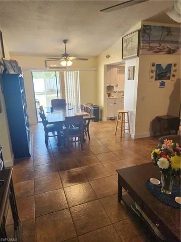 Open-concept living area featuring ceramic tile flooring, a dining space with a ceiling fan, and a pass-through opening to a kitchen with white cabinetry