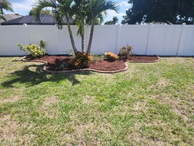 Expansive backyard featuring a white privacy fence, an established palm tree, and a mulched garden bed with brick edging