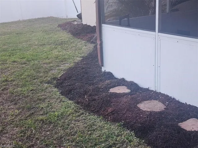 Screened enclosure exterior with a mulched landscape bed, stepping stones, and a white vinyl fence