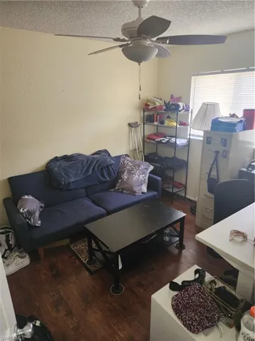 Living area featuring wood-finish flooring, a ceiling fan with integrated lighting, and a large window with blinds