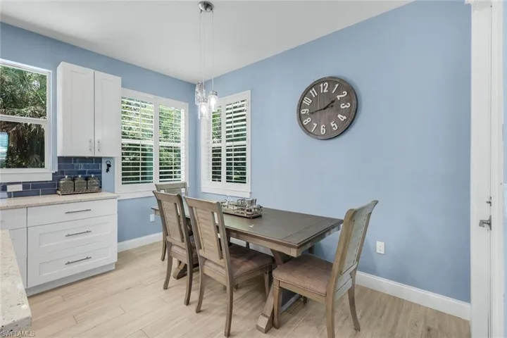 Kitchen and dining area featuring light wood-finish flooring, white cabinetry, a blue subway tile backsplash, and a pendant light fixture