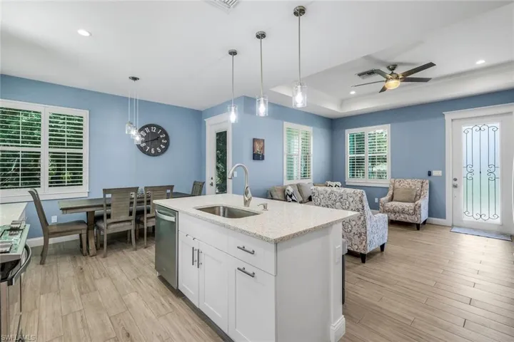 Kitchen island featuring a stainless steel sink, a pull-down faucet, and white cabinetry with brushed nickel hardware