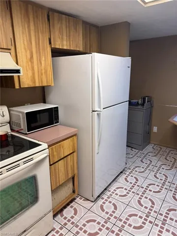 Kitchen with light tile patterned floors, white appliances, and ventilation hood