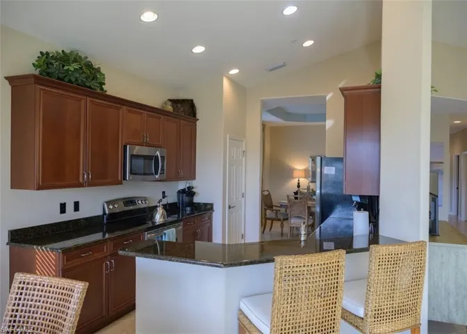 Kitchen featuring kitchen peninsula, a kitchen bar, stainless steel appliances, dark stone countertops, and lofted ceiling