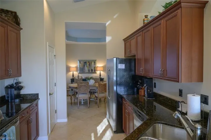 Kitchen with sink, dark stone countertops, lofted ceiling, light tile patterned floors, and appliances with stainless steel finishes