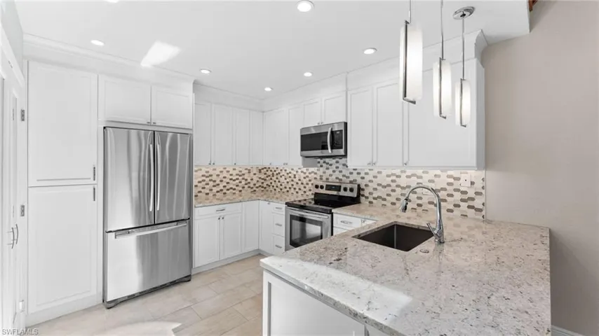 Kitchen featuring sink, hanging light fixtures, light stone counters, kitchen peninsula, and appliances with stainless steel finishes