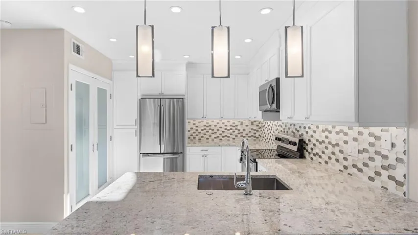 Kitchen featuring light stone counters, sink, stainless steel appliances, and decorative light fixtures