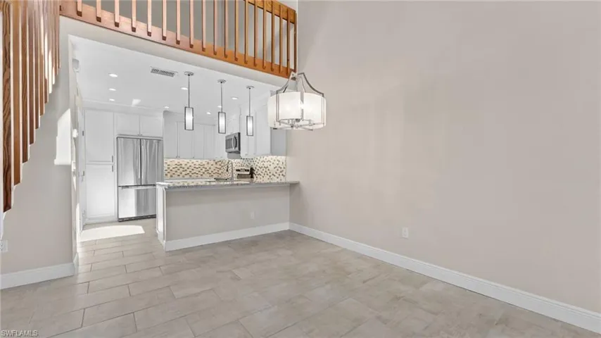 Kitchen with white cabinetry, stainless steel appliances, kitchen peninsula, decorative light fixtures, and decorative backsplash
