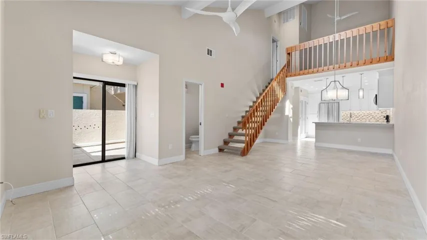 Unfurnished living room with beam ceiling, light tile patterned floors, high vaulted ceiling, and a chandelier