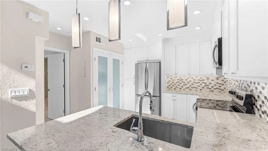 Kitchen with light stone countertops, sink, backsplash, white cabinets, and appliances with stainless steel finishes