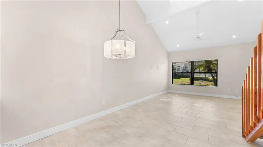 Unfurnished dining area with ceiling fan with notable chandelier and high vaulted ceiling