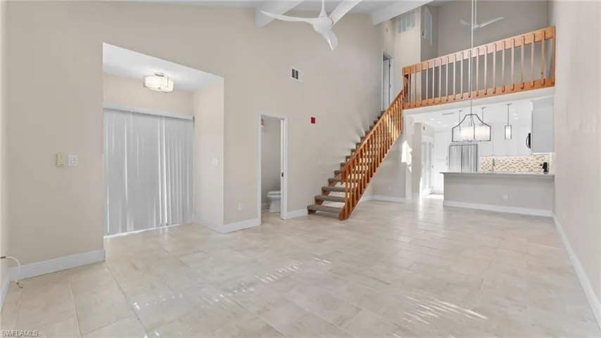 Unfurnished living room with beam ceiling, an inviting chandelier, and high vaulted ceiling