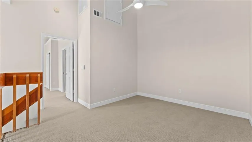 Empty room featuring light carpet, a high ceiling, and ceiling fan